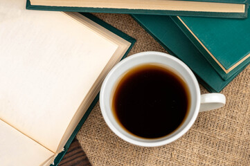 A cup of strong tea on a saucer and a stack of books on the table