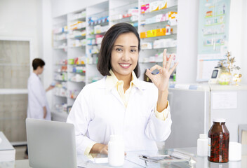    Asian  Female Confident Pharmacist  Looking Camera and Showing Ok Sign Hand Gesture in Pharmacy Shop or Drugstore Interior, Pharmaceutical Store Concept