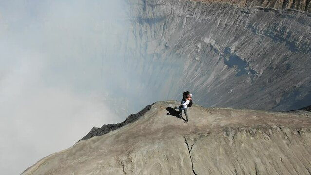 Aerial View of Man and Woman Embracing on Ridge Active Volcano. Girl Waving to Camera. Mount Bromo (Gunung Bromo) in East Java, Indonesia