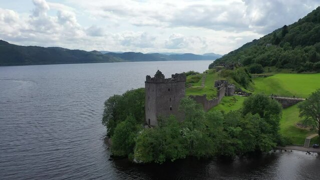 Captivating drone shot of Urquhart Castle on Loch Ness in Scotland. The shot sweeps low to the water and rises high above the castle, revealing the beautiful scenery.