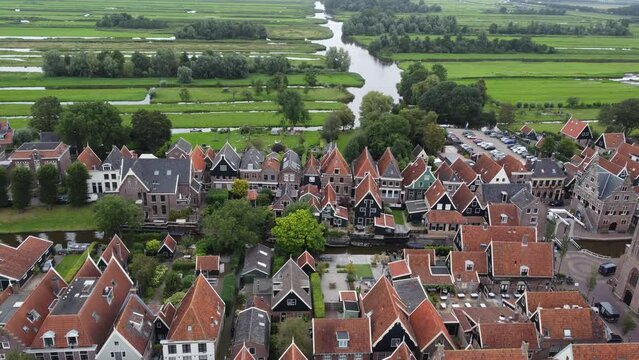 Aerial view of a small Dutch village surrounded by farms and canals. Tall, narrow homes and cars line the streets and small rafts drift along the canals. Animals graze as we glide into the horizon.