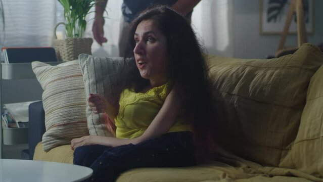 Irritated husband talking and yelling at wife with a physical disability who is sitting on a sofa during quarrel at home