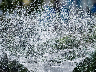Plakat Splashes of water on dark background. Water sprays in sunny day close-up.