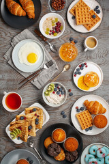 Fototapeta na wymiar Continental breakfast captured from above (top view, flat lay). Coffee, tea, croissants, jam, egg, pancakes, maffins and oatmeal. Wooden background. Family breakfast table.