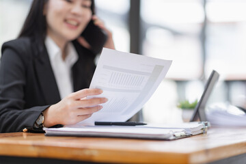 Obraz premium Business Asian woman talking on the phone and working with laptop calculator document on an office desk, planning analyzing the financial report, business plan investment, finance analysis concept.