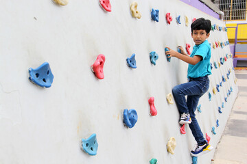 Latin dark-haired male child with blue t-shirt practicing sports wall climbing without fear of heights and exercising
