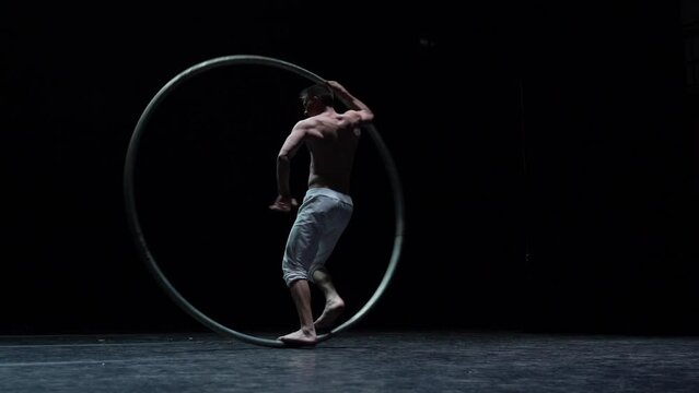 Muscular circus artist perform Cyr Wheel on a black background. Concept of originality, creativity and outstanding