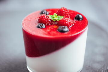 Panna cotta dessert with sauce from berries. Cherries, raspberries and blueberry as decoration. Served in two glasses on dark background. Traditional Italian creamy dessert.