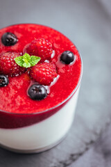Panna cotta dessert with sauce from berries. Cherries, raspberries and blueberry as decoration. Served in two glasses on dark background. Traditional Italian creamy dessert.
