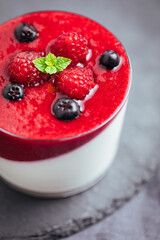 Panna cotta dessert with sauce from berries. Cherries, raspberries and blueberry as decoration. Served in two glasses on dark background. Traditional Italian creamy dessert.