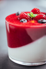 Panna cotta dessert with sauce from berries. Cherries, raspberries and blueberry as decoration. Served in two glasses on dark background. Traditional Italian creamy dessert.