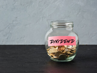 Glass jar with coins and the word dividend on a label. Business finance investment, distribution of profits or dividend tax - obrazy, fototapety, plakaty