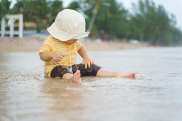 Cute Asian baby boy wearing hat sitting playing on the sand beach.