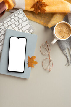 Autumn business concept. Top view vertical photo of smartphone over planner spectacles fallen maple leaves keyboard cup of frothy coffee and plaid scarf on isolated grey background with empty space