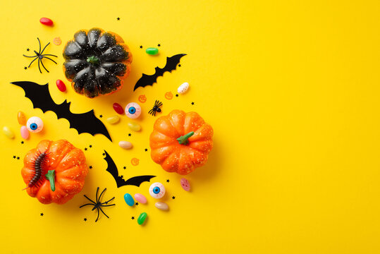 Halloween concept. Top view photo of pumpkins bat silhouettes spooky eyes centipede candies spiders and confetti on isolated yellow background