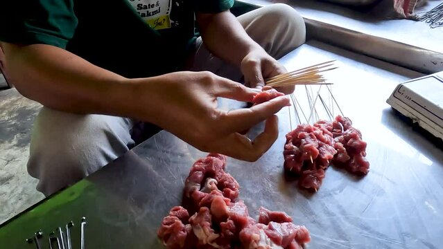 Preparing traditional Indonesian dish satay, close up on chef stabbing mutton on wooden sticks