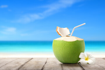 Cool coconut juice on wood table  with sandy beach background.