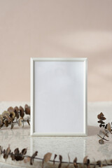 blank white photo frame mockup with eucalyptus brancch at peach wall