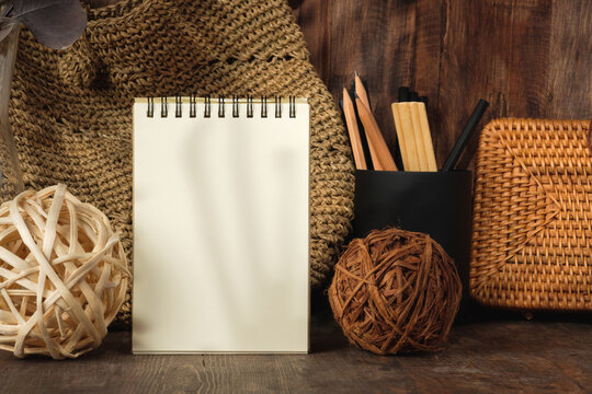blank sprial notebook with wicker bag and travel stuff on table with sunlight