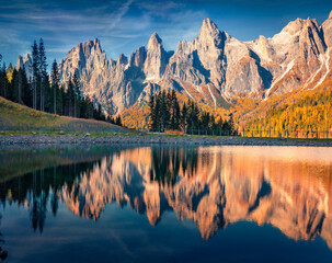 Fototapeta na wymiar Pala di San Martino Mountain Range reflected in the calm waters of Malga Ces Lake. Gorgeous autumn view of Dolomite Alps. Astonishing outdoor scene of Italy. Beauty of nature concept background.