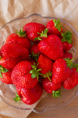 Many red strawberries on glass plate and wooden table top view