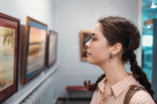 Portrait of a pretty young woman looking at a painting. An exhibition in an art gallery. Excursion and visit to the museum