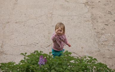 a blonde girl stands near a lilac bush and shows a wand

