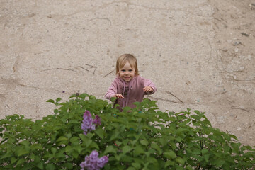 a child in a lilac jacket stands near the greenery and laughs
