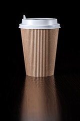 Disposable paper cup made of brown corrugated cardboard with a white lid on a black background.