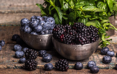 Juicy fresh blueberries and blackberries in bowls with mint leaves