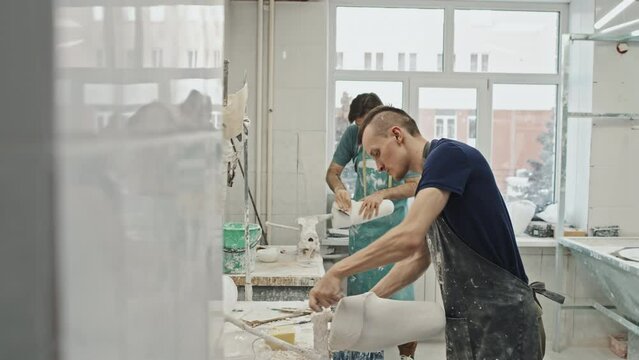 Two young adult Caucasian men working with plaster casts for prosthetic leg sockets, removing extra materials and polishing