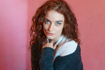 Pretty young woman against pink exterior wall with copy place on city street, red curly hair in a white shirt and a gray jacket looks at the camera