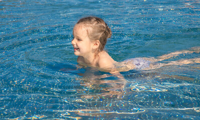 Happy girl swims in the pool. Child learn to swim. Holidays for children. Happy healthy lifestyle. Summer sports. Relaxation and rest.
