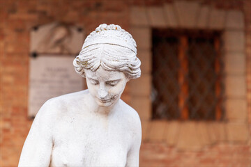 Mezzo busto di statua di donna in stile romano con sfondo una facciata in mattoncino di edificio...