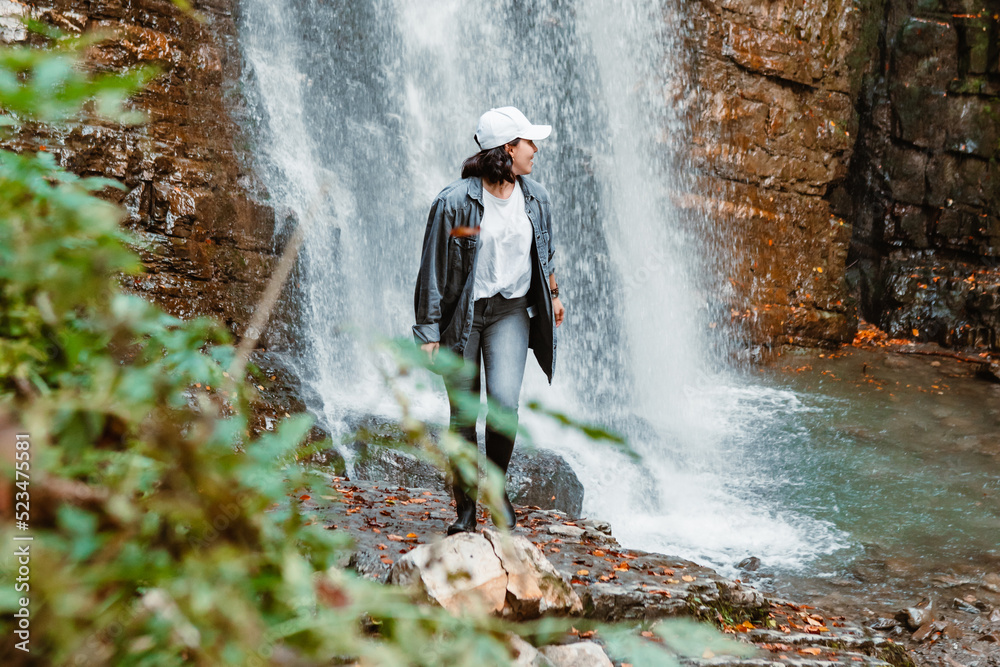 Wall mural young pretty woman hiking enjoying view of waterfall