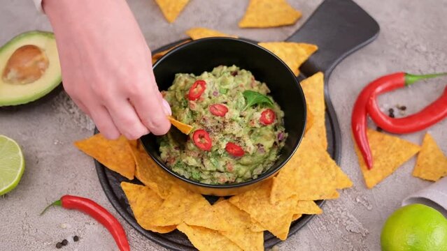 woman dips nachos chips to freshly made guacamole dip sauce in marble bowl mortar