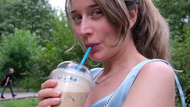 Happy woman drinking ice latte in a park