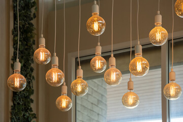 Vintage tungsten filament multiple lamps hanging from the ceiling on a white wires as an interior...