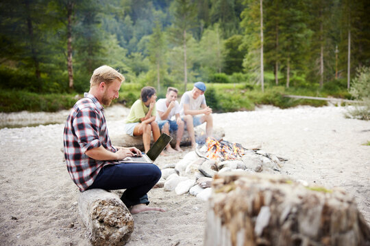 Businessman using laptop sitting on log with friends in background