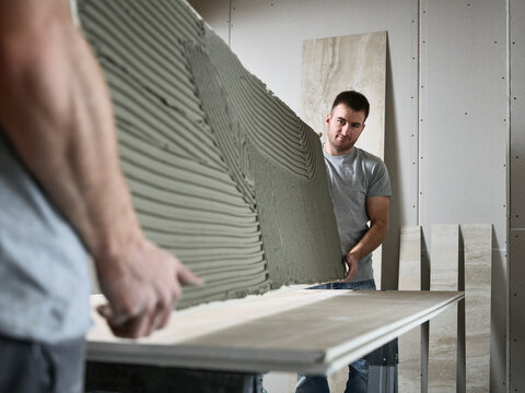 Tilers holding ceramic tile at table on construction site