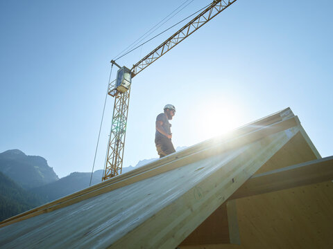 Carpenter standing on roof at construction site under clear sky