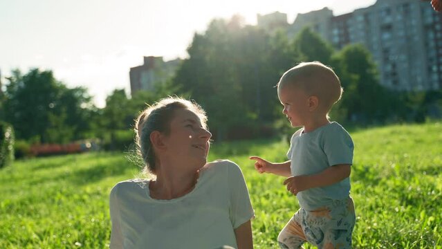 Happy toddler boy plays with women in park. Child touches noses of mother and aunt and runs on grass. Boy child enjoys playing on picnic lawn slow motion closeup