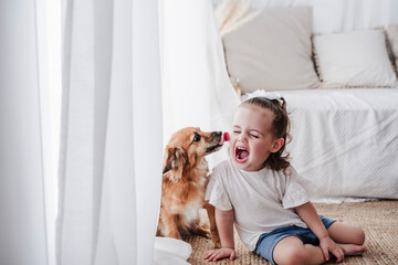 Dog licking little girl face at home