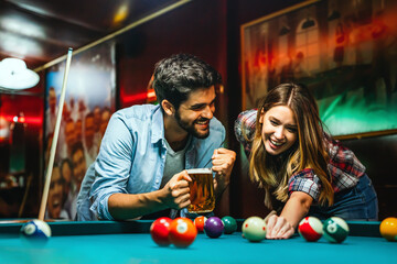 Happy young couple enjoying while playing billiard in bar. People entertainment fun concept