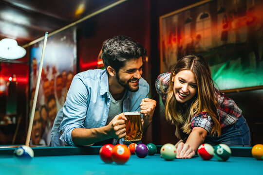 Happy young couple enjoying while playing billiard in bar. People entertainment fun concept - Powered by Adobe