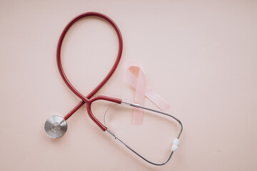 Fototapeta premium Pink ribbon and stethoscope on a pink background. Top view. Breast cancer awareness concept