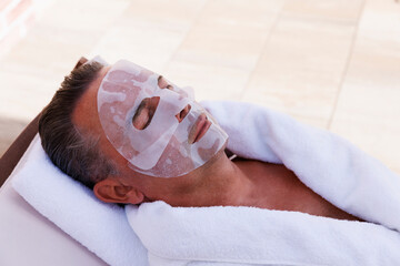 Mature man with facial mask relaxing at pool spa