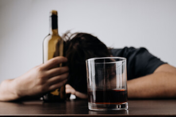 Man with glass and bottle of whiskey lying or sleeping on table. Alcohol addiction concept