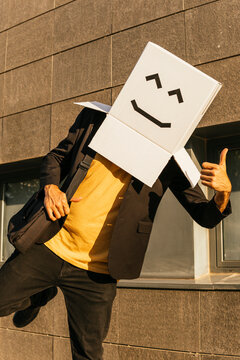 Businessman Wearing Box With Smiley Face Showing Thumbs Up On Sunny Day