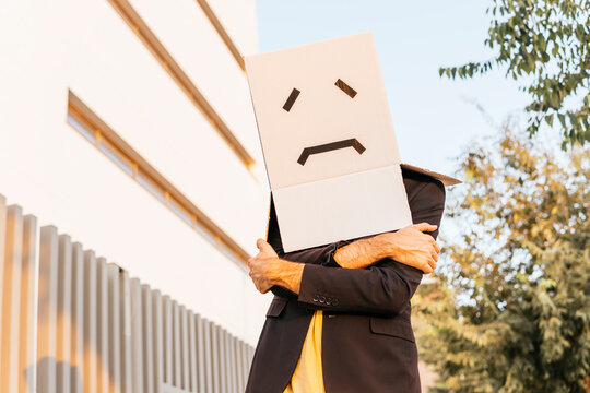 Man wearing box with sad face standing with arms crossed